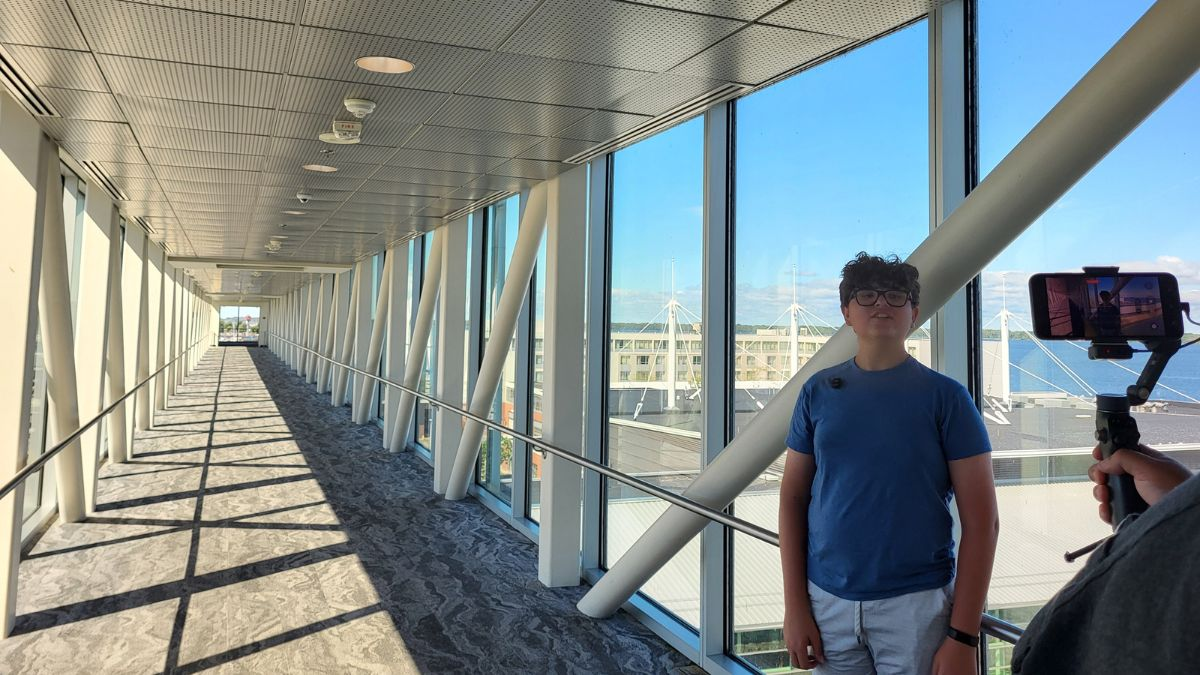 Teen recording travel content on a glass skybridge connecting buildings near the Erie Bayfront