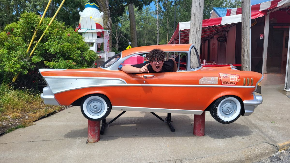 Teen posing inside a vintage orange classic car display outside Sara’s Diner in Erie, Pennsylvania